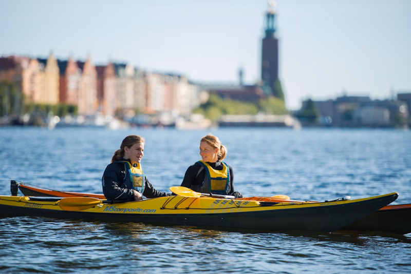 2 personer som paddlar kajak på Riddarfjärden i Stockholm. De är ute och paddlar runt kungsholmen på en härlig kajaktur.